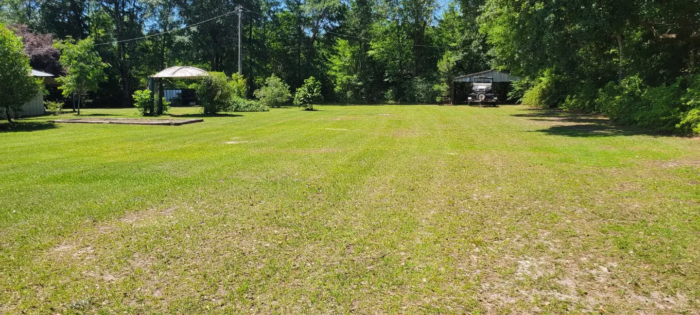 A wide rural property in the Florida Panhandle, freshly mowed by Faith Lawn Care, with mowing stripes running the length of the yard toward a treeline