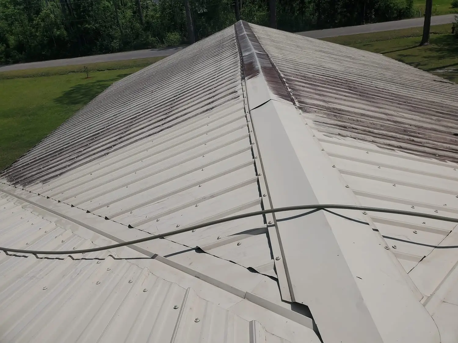 A close look down a metal roof mid-wash, the cleaned panels bright against the brown streaking still left on the unwashed sections